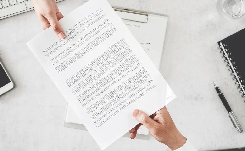 Mani che consegnano un documento contrattuale su una scrivania da ufficio, simbolo della sottoscrizione di un abbonamento