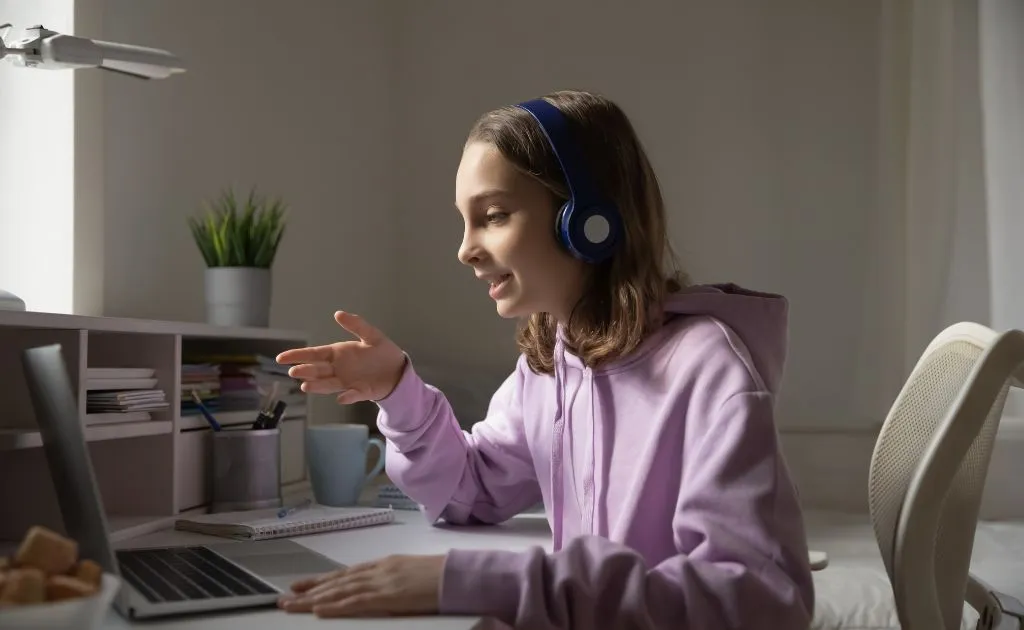 Studentessa con cuffie segue una lezione di ripetizioni online al laptop da casa