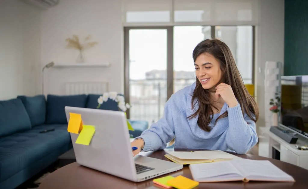 Studentessa sorridente studia al laptop con quaderno aperto, confrontando piattaforme di ripetizioni online